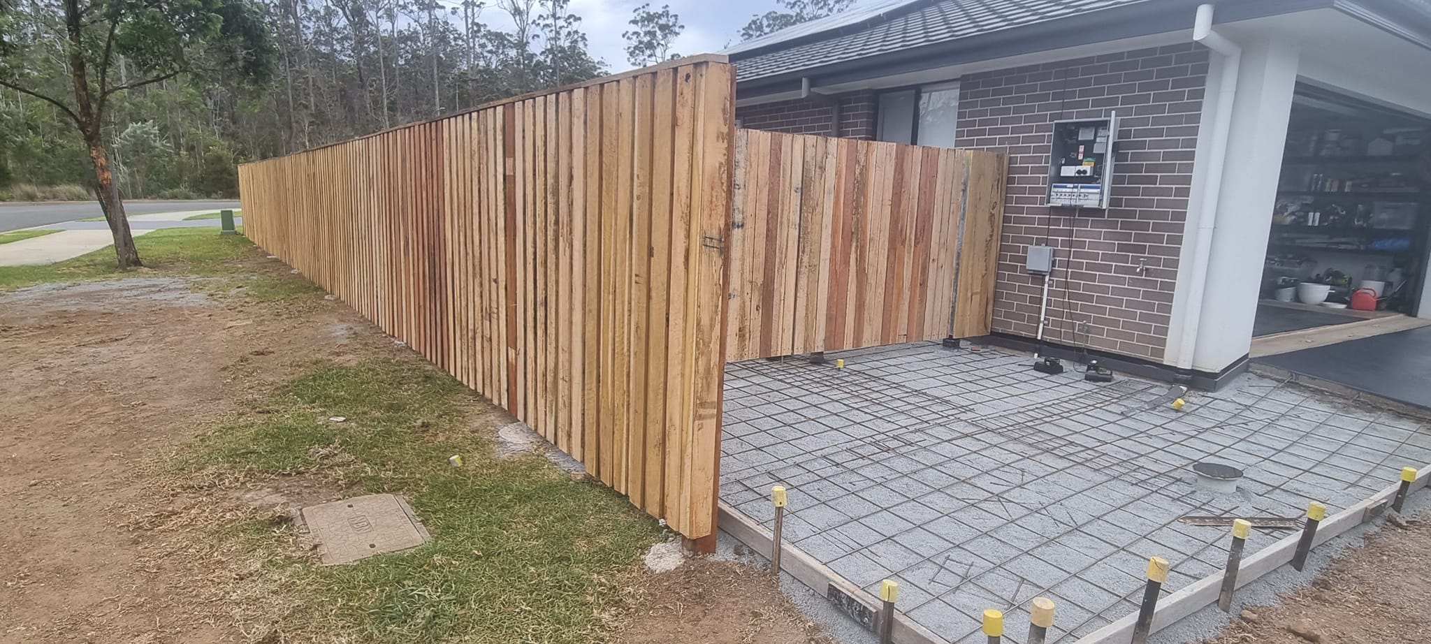 Hardwood paling fence beside brick home and concrete slab