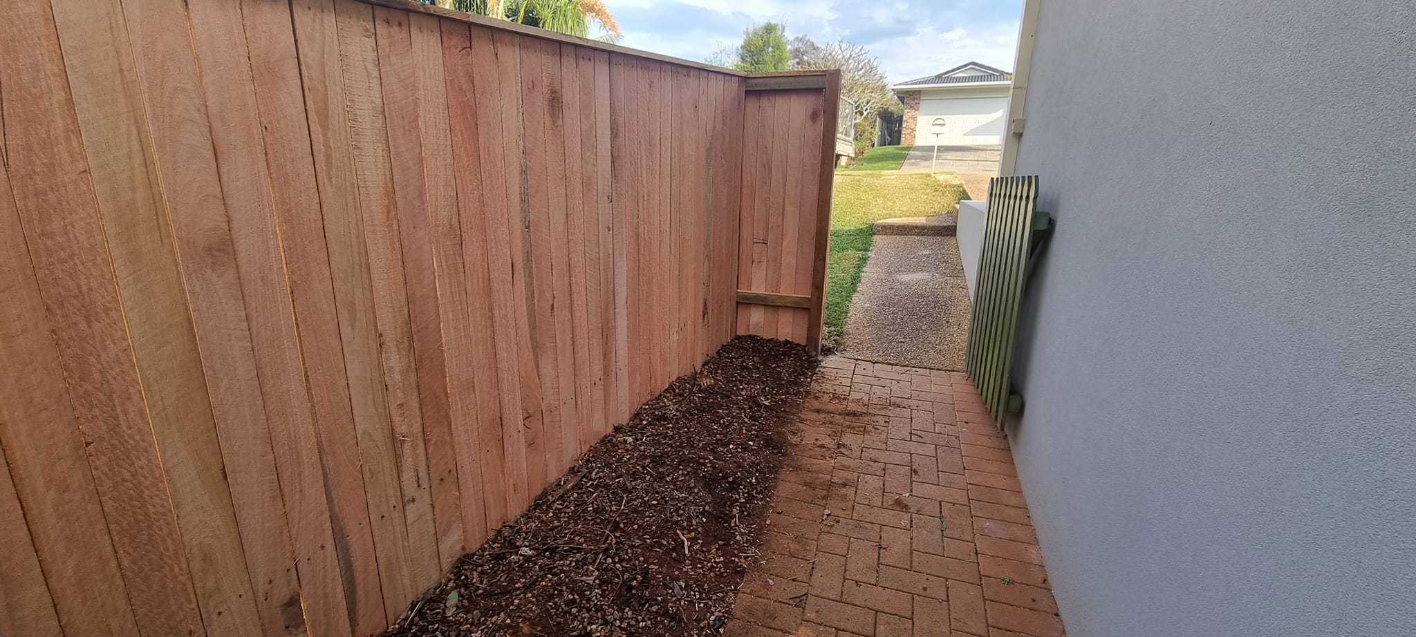 Tall hardwood paling fence beside brick path